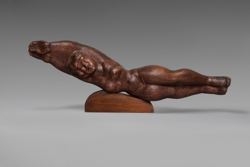 Medium dark wood sculpture of a female form lying on its side in a diving like position. The arms and legs are both conjoined together and her waist is raised slightly off of the small wood mount. 