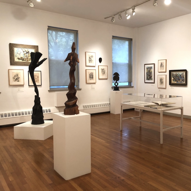 Exhibition installation photo showing various sculptures and framed drawings. There is a case with books and two sculptures by Chaim Gross in the center.